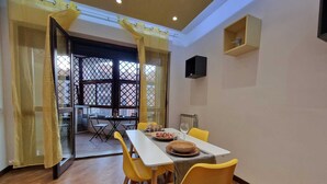 A dining area with a table set for two, yellow chairs, and a view through a window with a lattice design. - Cozy and Comfortable Apartment near Fiumicino Airport (Lazio)