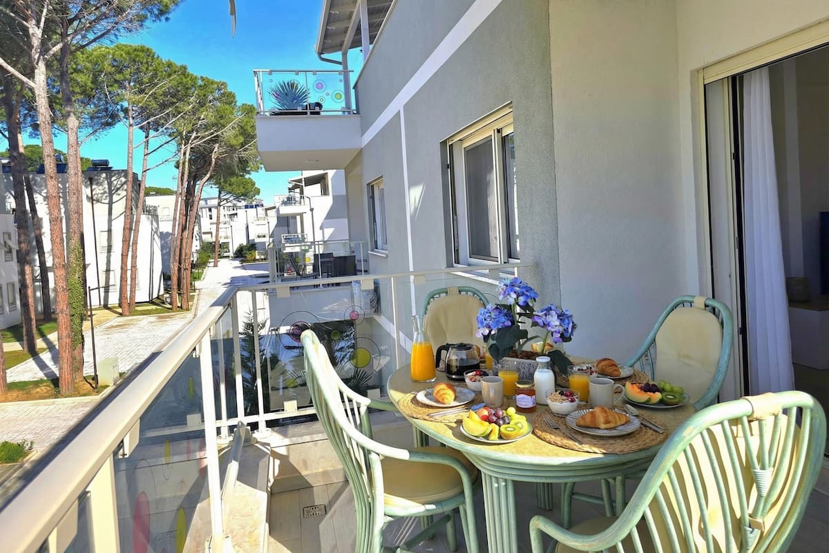 A balcony with a table set for breakfast, including fruits, pastries, and beverages.