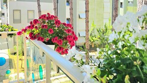 Un balcon avec une balustrade, des plantes en pot et une vue sur les immeubles.