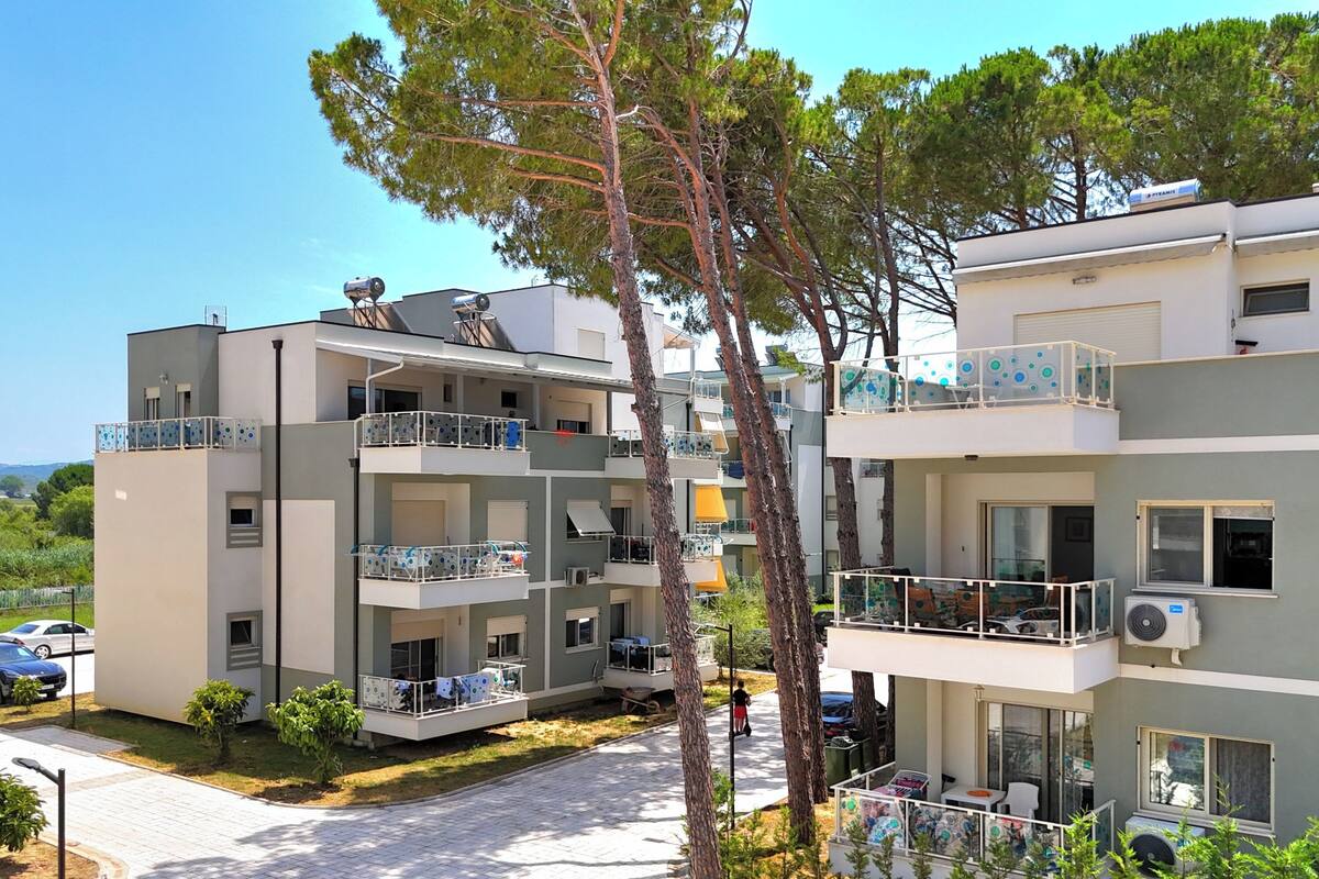 A multi-story residential building with balconies, outdoor seating, and a clear sky.