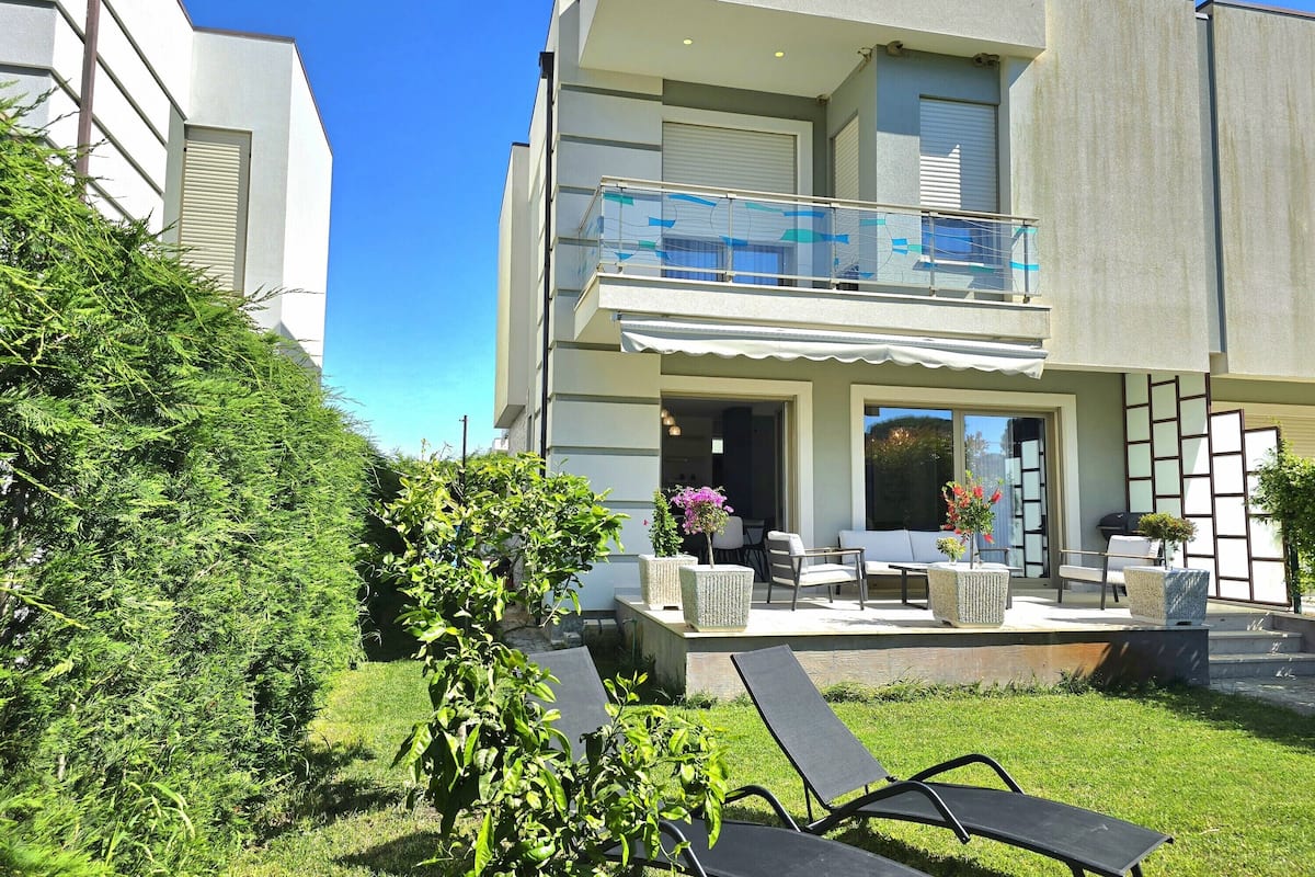 A modern two-story house with a balcony, outdoor seating area, and a well-maintained garden.