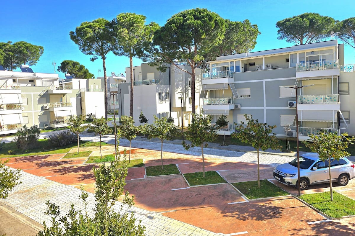 A residential building with multiple balconies, a parking area, and trees.