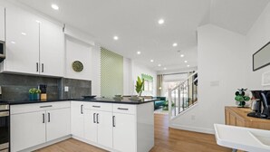 A modern kitchen with white cabinets, a black countertop, and a green plant.