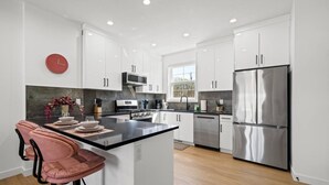 A modern kitchen with white cabinets, stainless steel appliances, a central island, and a red clock on the wall. - Pretty in Pink | Hot Tub | 10 min to WEM | KingBed (Edmonton)