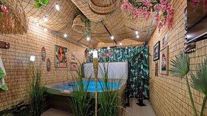 A spa area with a hot tub, bamboo walls, and tropical plants. - Pretty in Pink | Hot Tub | 10 min to WEM | KingBed (Edmonton)