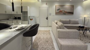 Une cuisine moderne avec des meubles blancs, un coin repas doté d’un tabouret de bar, un canapé et une table basse.