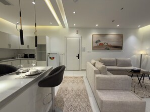 A modern kitchen with white cabinets, a dining area with a bar stool, a sofa, and a coffee table.