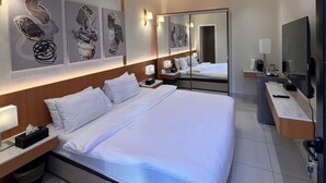 Une chambre d’hôtel moderne avec un grand lit, des tables de chevet, une télévision et des œuvres d’art accrochées aux murs.