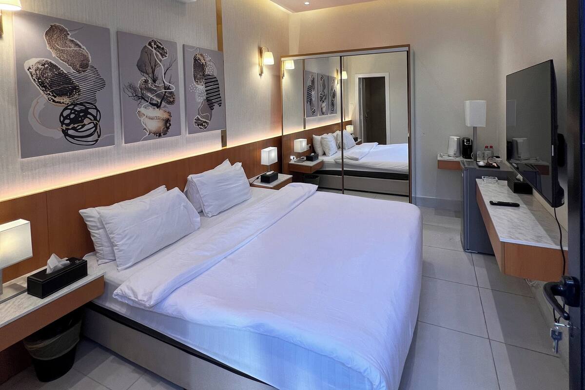 A modern hotel room with a large bed, bedside tables, a TV, and artwork on the walls.