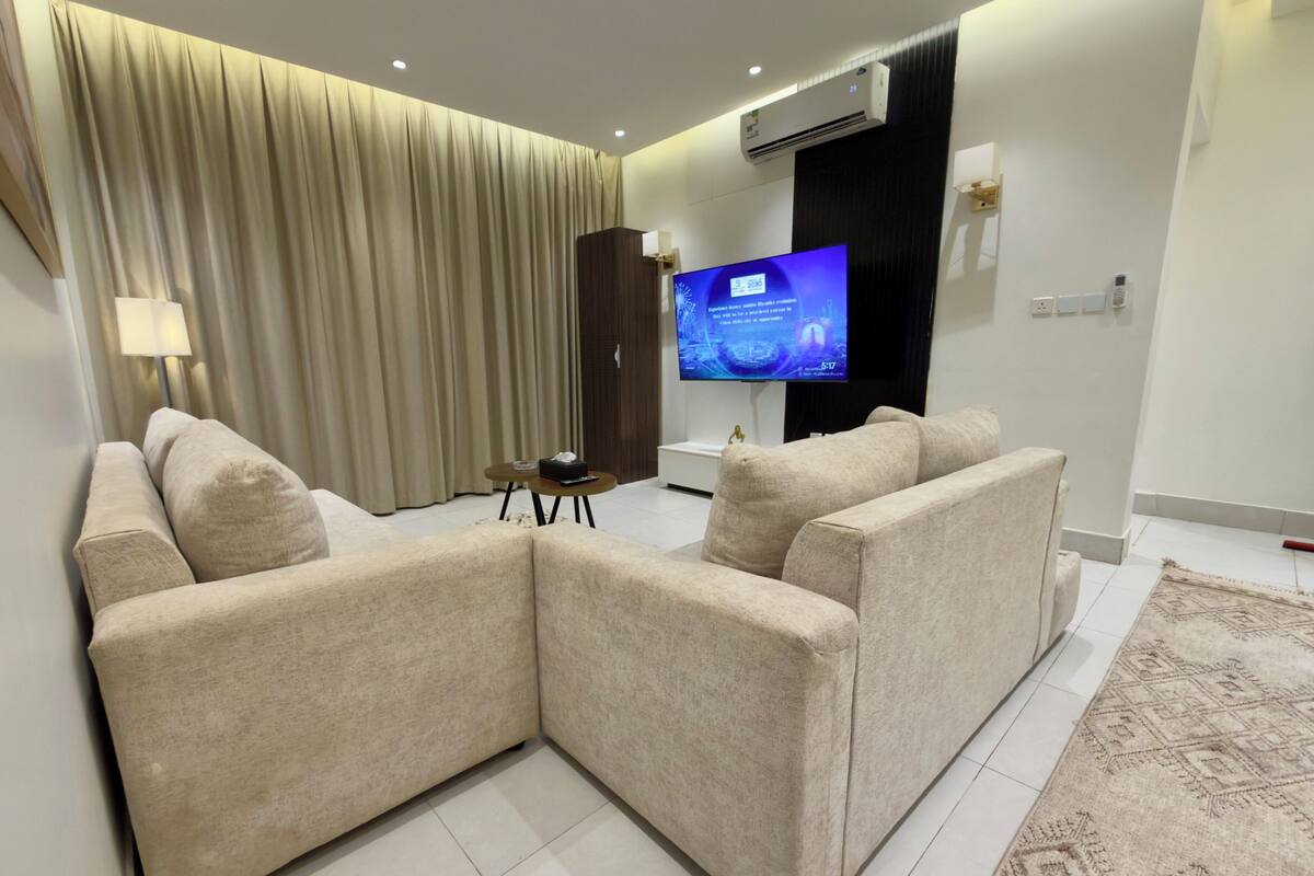 A modern living room with a sectional sofa, a flat-screen TV, and a large window with curtains.