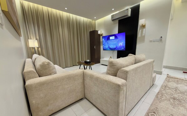 A modern living room with a sectional sofa, a flat-screen TV, and a large window with curtains. - Riyadh Luxury (Riyadh)