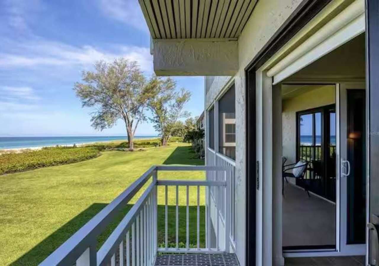 Ein Balkon mit Meerblick, eine Rasenfläche und eine Tür zu einem Zimmer mit einem Sessel.