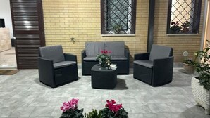 A patio area with three wicker chairs and a central table, set against a brick wall with windows. - Greta family house: Victory (Roma)