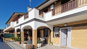 A two-story residential building with a covered patio area, outdoor seating, and potted plants. - Greta family house: Victory (Roma)