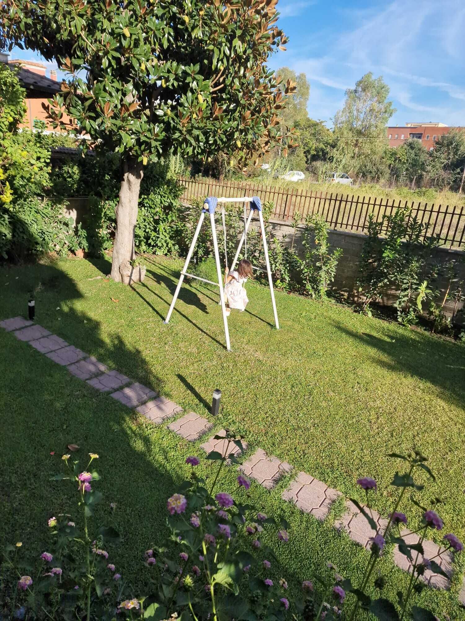 A grassy yard with a swing set, a tree, and a brick pathway.