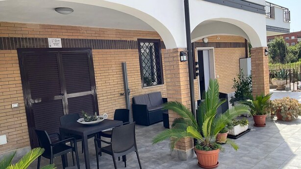 An outdoor patio area with a table and chairs, surrounded by potted plants and a brick wall. - Greta family house: Victory (Roma)