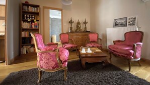 Un salon doté d’une cheminée, d’une bibliothèque et d’un coin repas avec des chaises recouvertes d’un tissu rose et une table basse.