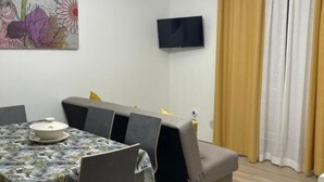 A dining area with a table set for four, a sofa, and a television mounted on the wall. - Greta family house: Luke (Roma)