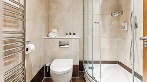 Un baño moderno con ducha de vidrio, inodoro y repisa con artículos de aseo.