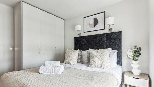 Un dormitorio moderno con una cama grande, un cabecero oscuro y una mesita de noche con un jarrón.