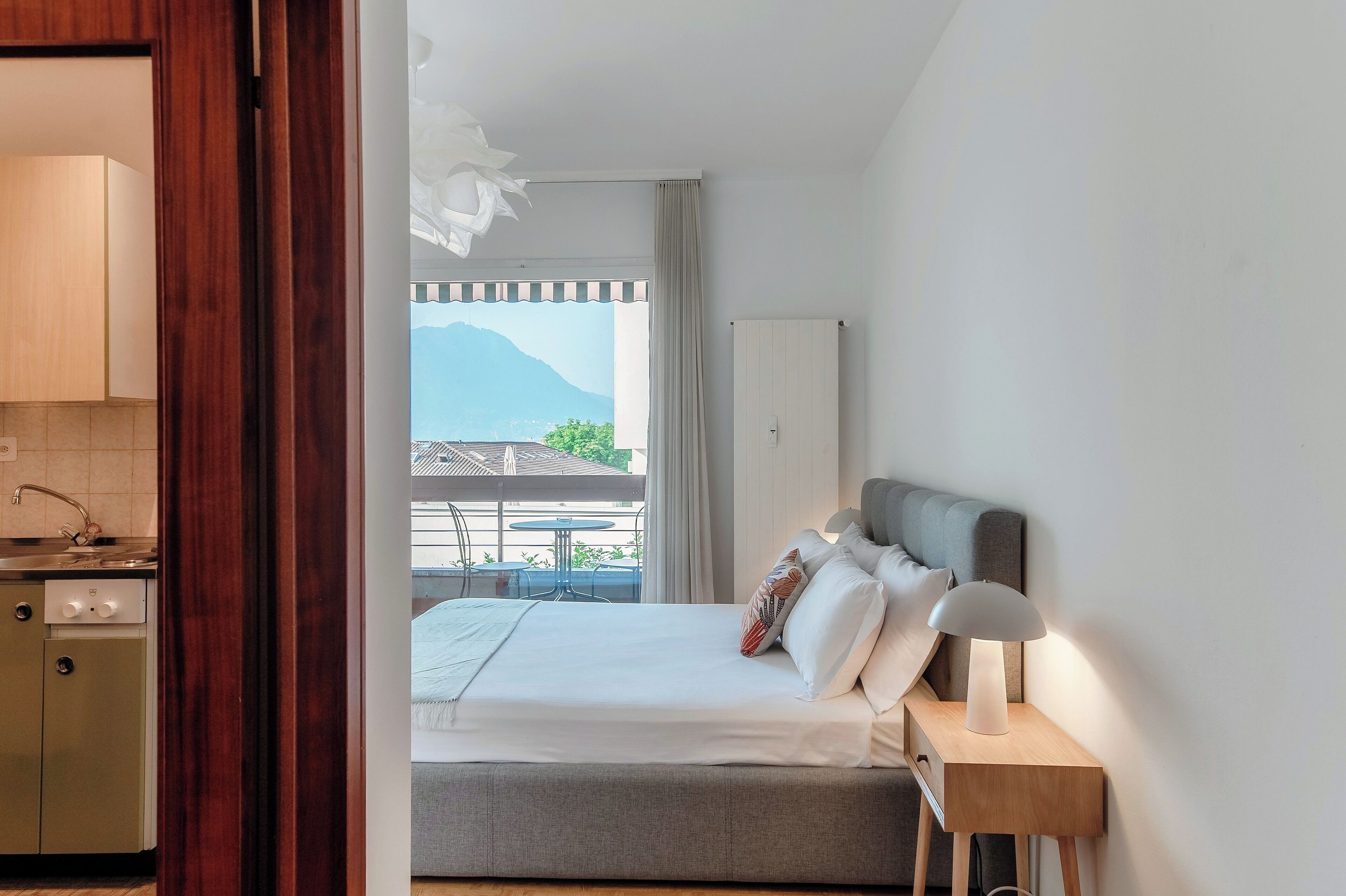 A hotel room with a bed, bedside lamp, and a view of mountains through the window.