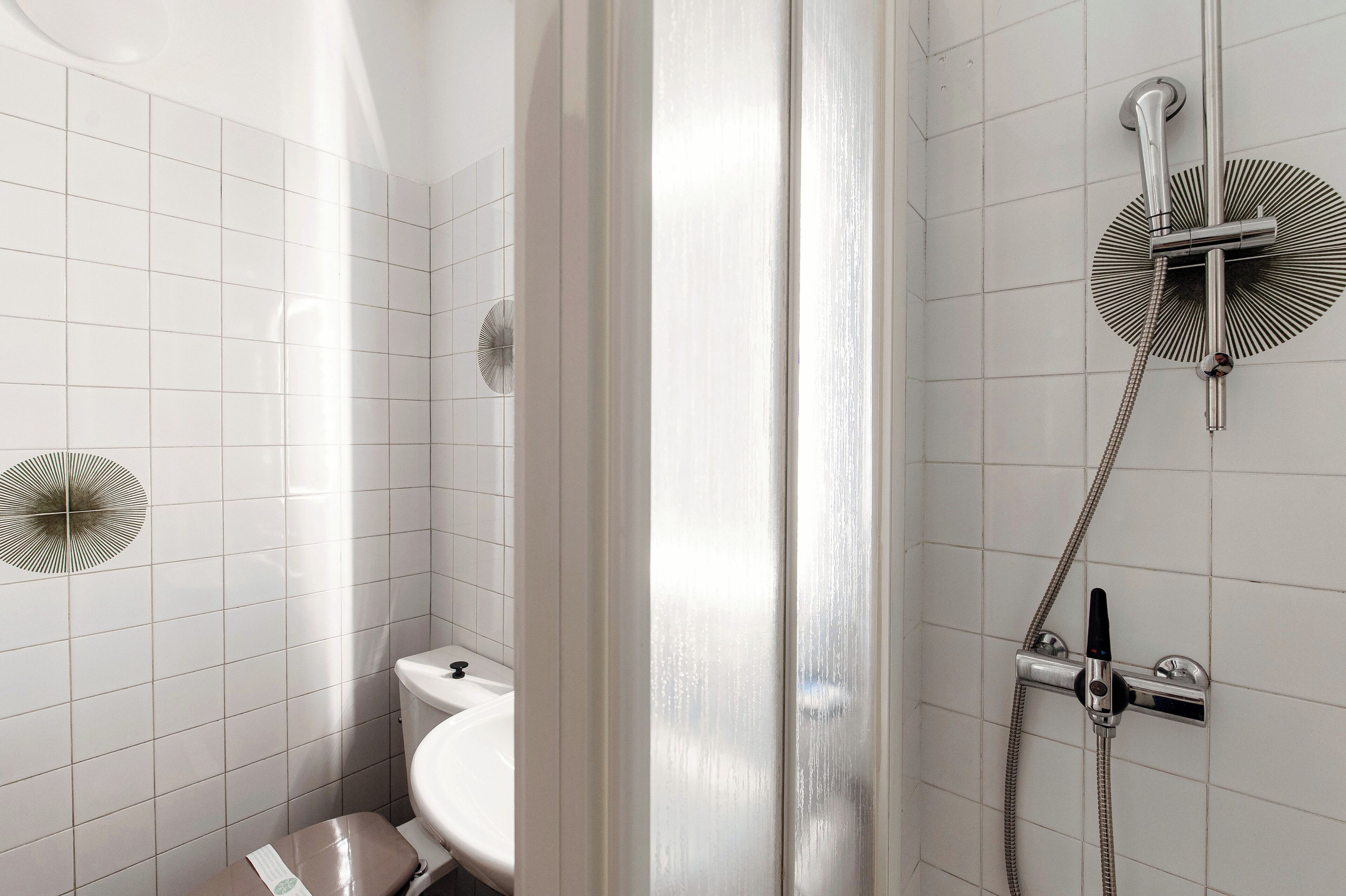 A bathroom with white tiled walls, a toilet, and a shower with a handheld showerhead.