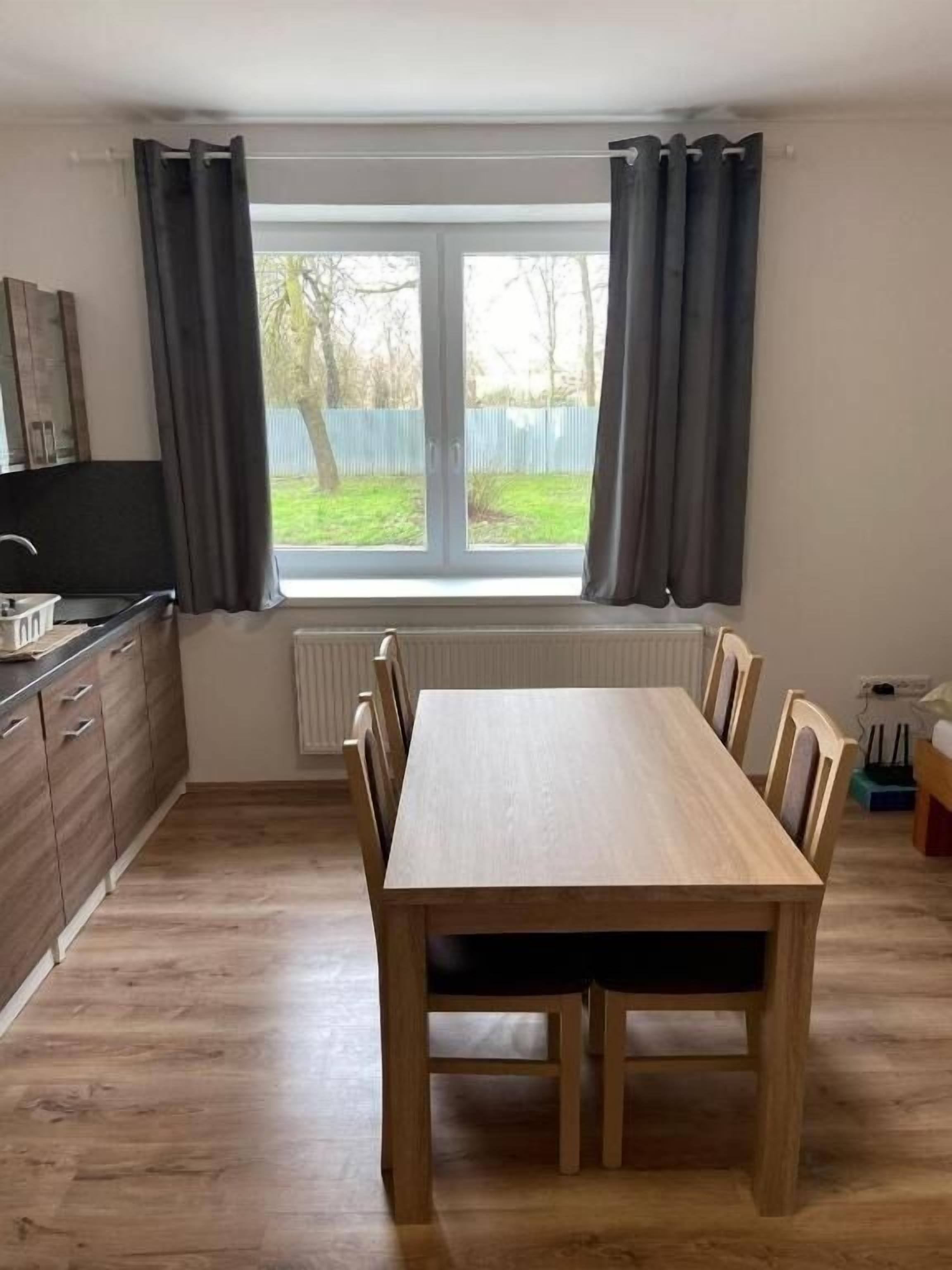 A kitchen with a dining table and chairs, a window with curtains, and a view of the outdoors.