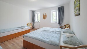 Una habitación con dos camas individuales, suelo de madera, una lámpara en el techo y una ventana con cortinas.