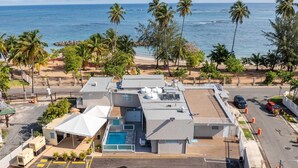 Un hotel con piscina en la azotea, zona de estacionamiento y vistas a la playa y al océano.