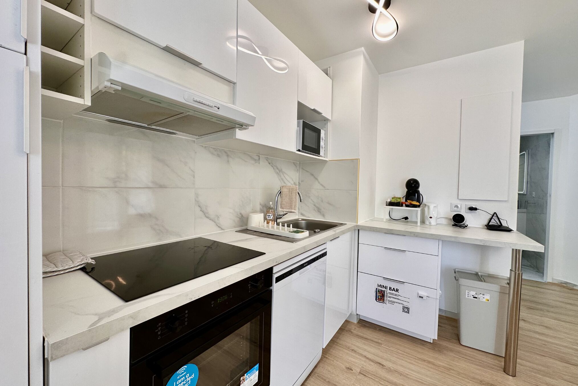 Une cuisine moderne avec des meubles blancs, un four à micro-ondes encastré, un lave-vaisselle et une plaque de cuisson à induction noire.