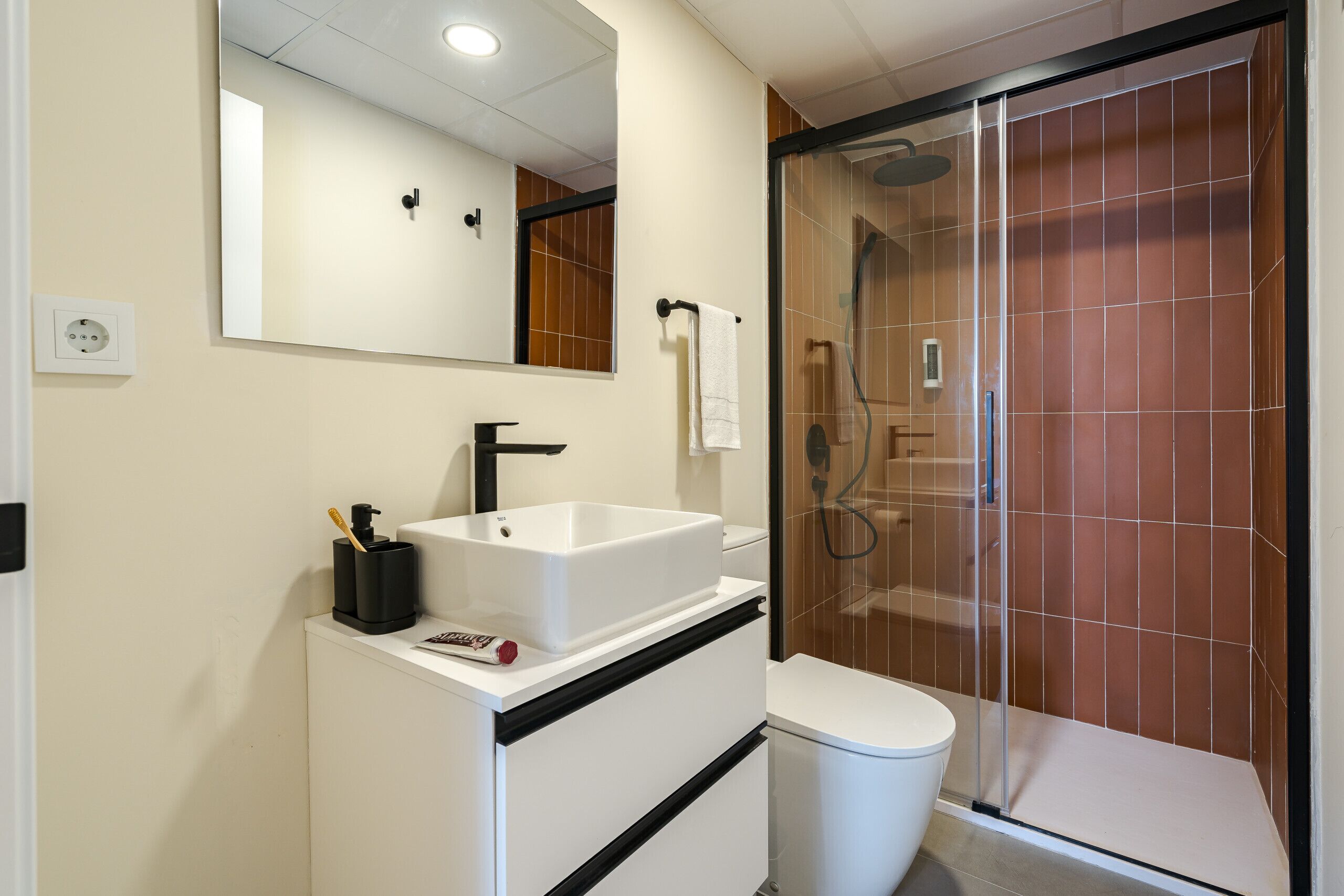 A modern bathroom with a white sink, black faucet, and a glass-enclosed shower.
