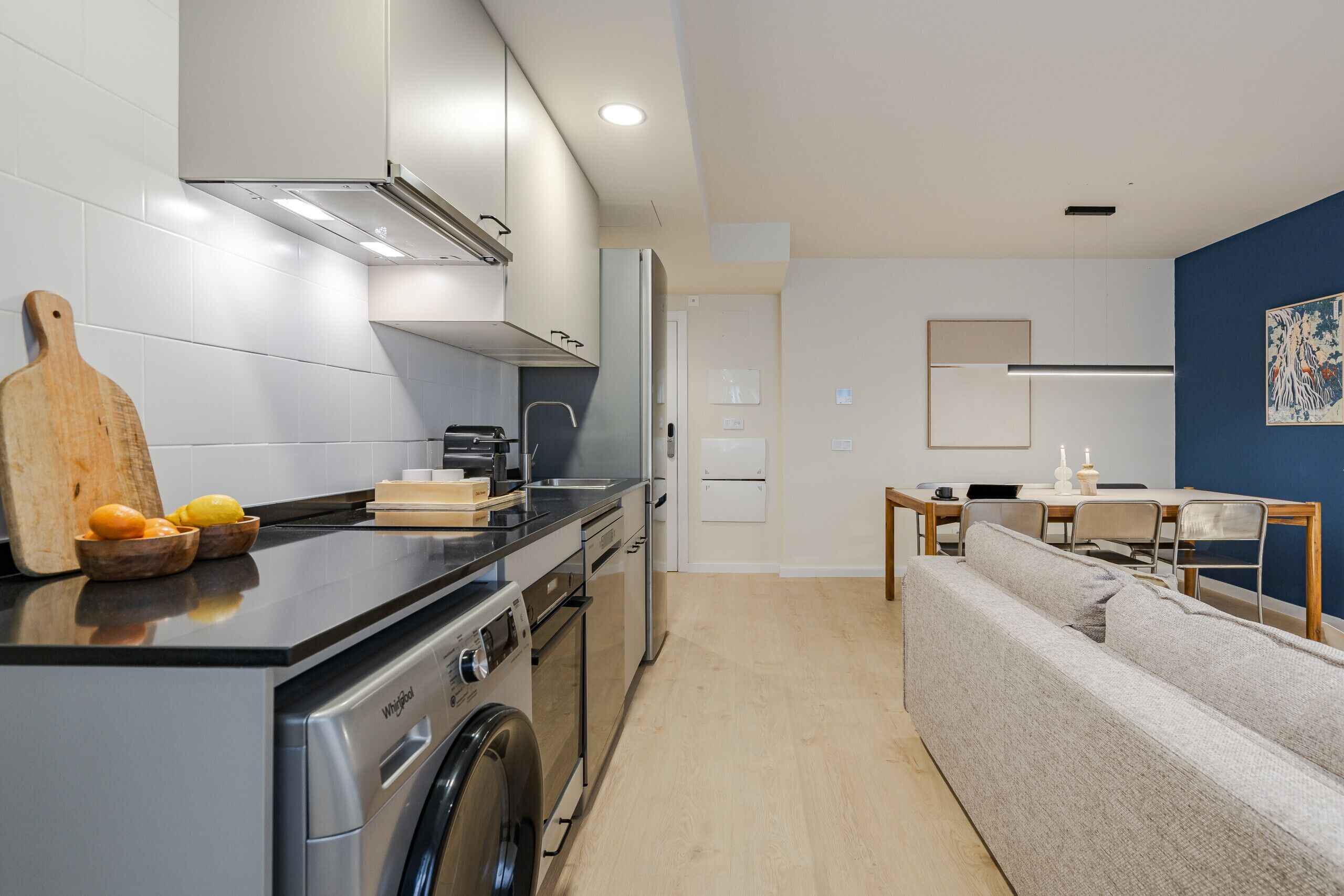 Une cuisine moderne équipée d’un lave-linge et d’un sèche-linge intégrés, un coin repas avec une table et des chaises, et un espace de vie avec un canapé.