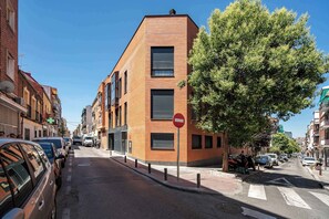 A street view with a modern building, parked cars, and a no-entry sign. - Puerto Alto Apartments by Olala Homes (Madrid)