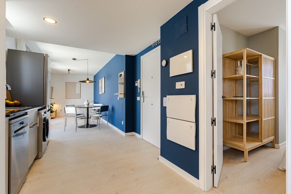A modern kitchen with stainless steel appliances, a dining area with a table and chairs, and a built-in wooden shelving unit.