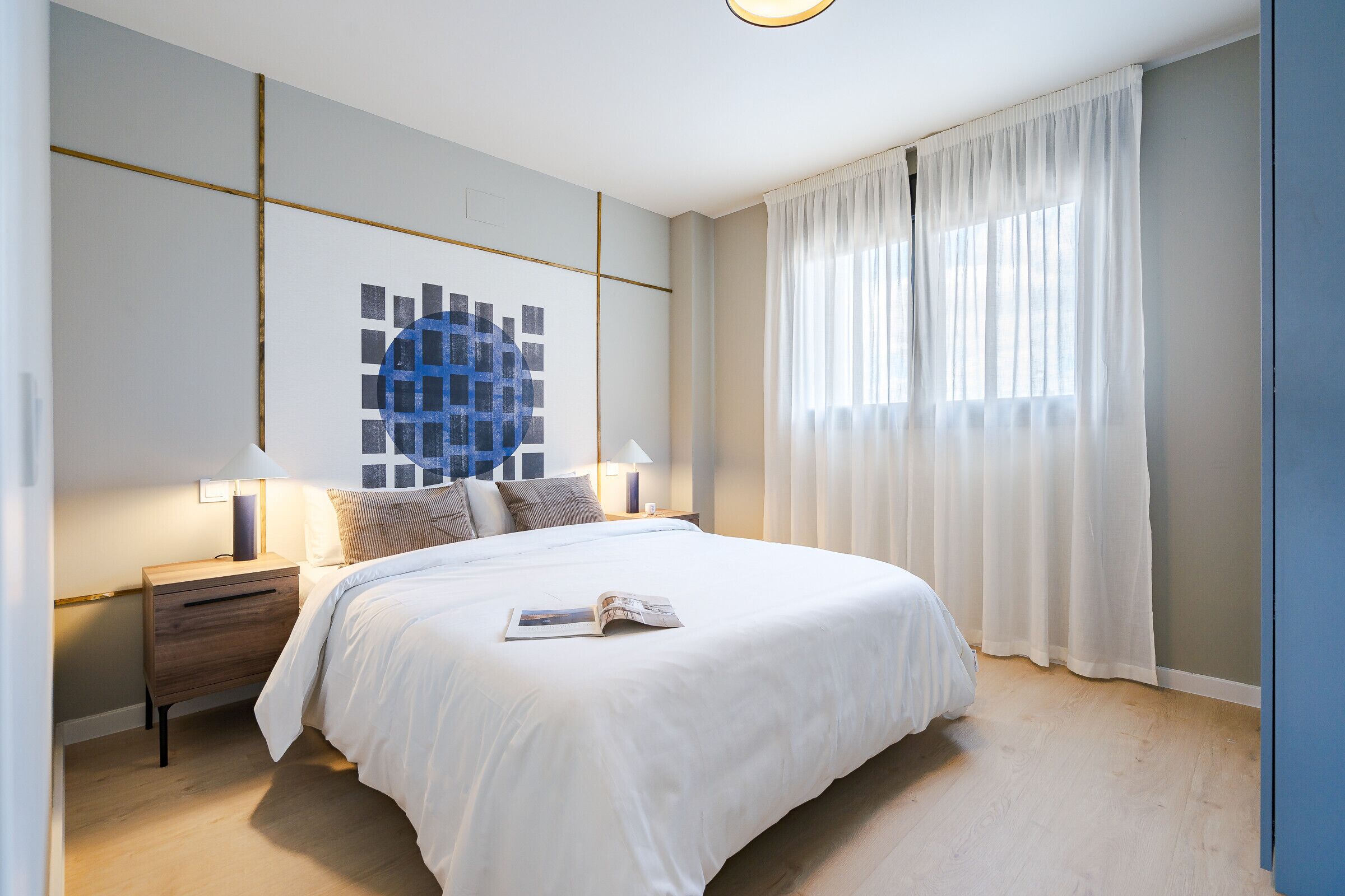 A modern bedroom with a large bed, a nightstand, a lamp, and a wall art piece.
