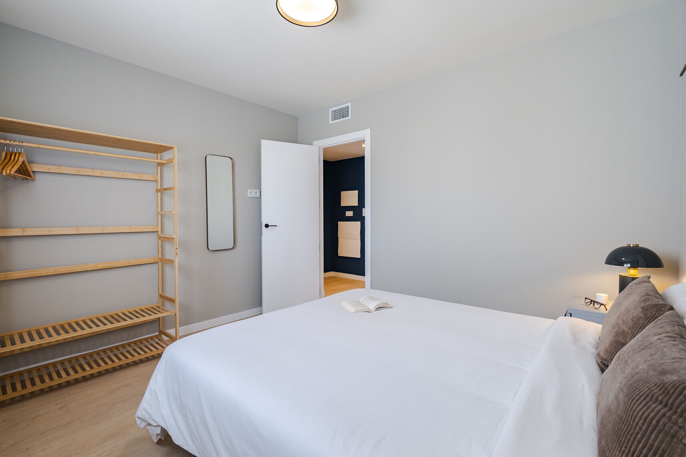 Ein Schlafzimmer mit einem Bett, einem Holzschrank, einer Tür zu einem anderen Raum und einem Nachttisch mit Lampe.