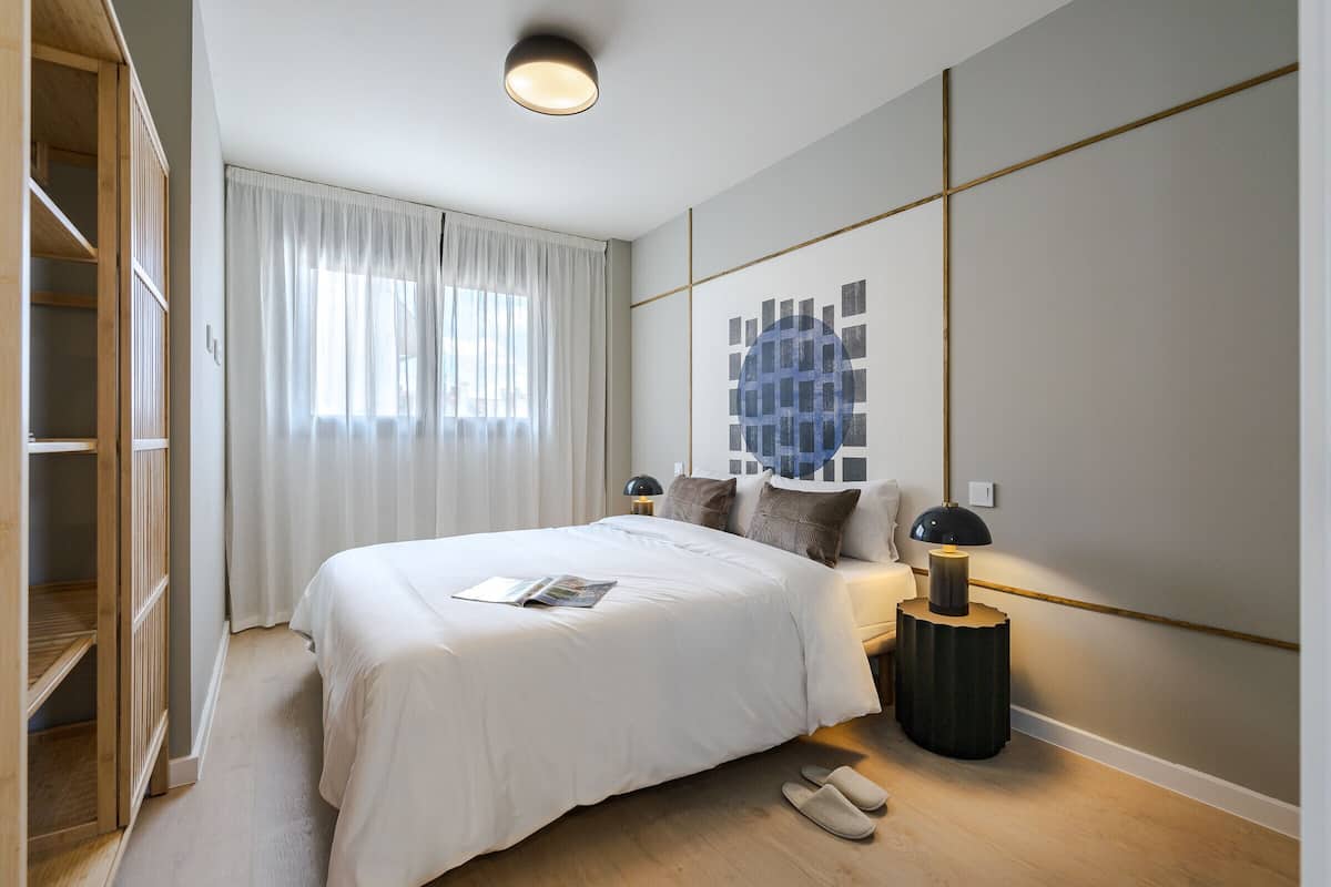 Une chambre à coucher moderne avec un grand lit, des lampes de chevet et une vue sur la ville par la fenêtre.