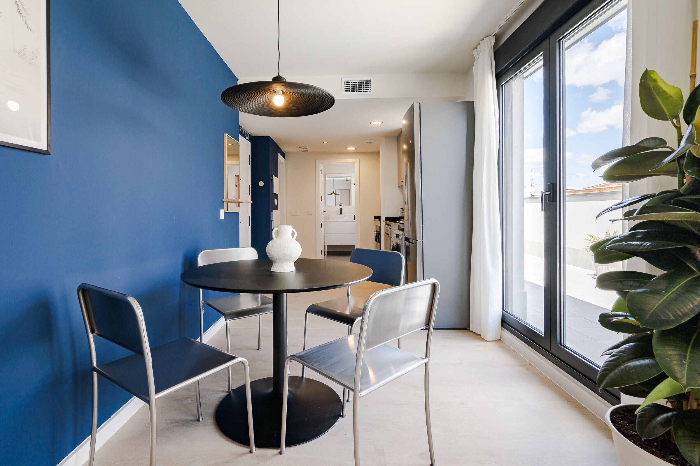 A dining area with a round table, four chairs, a pendant light, and a potted plant.
