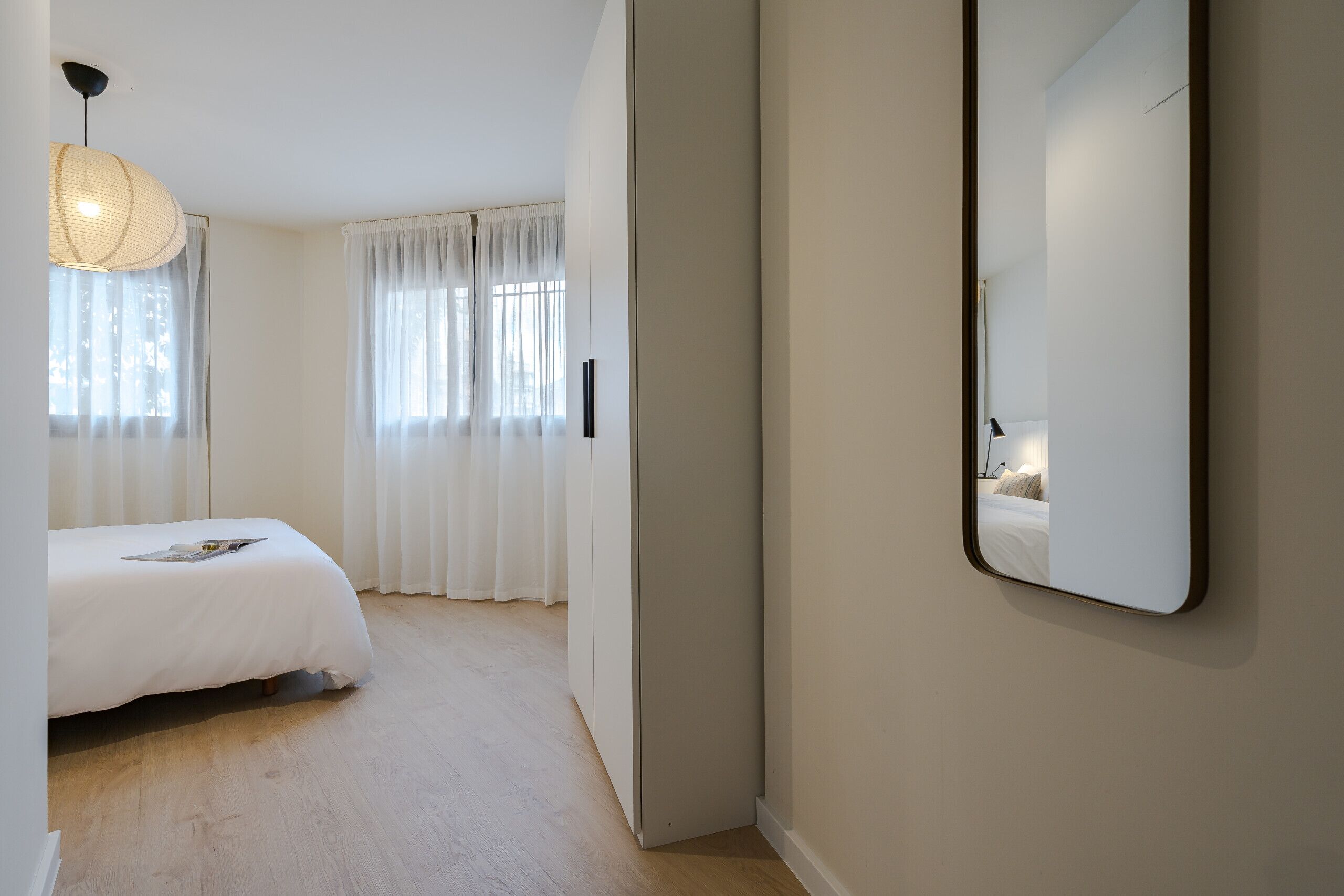 Un dormitorio con cama, lámpara de noche y un espejo grande en la pared.
