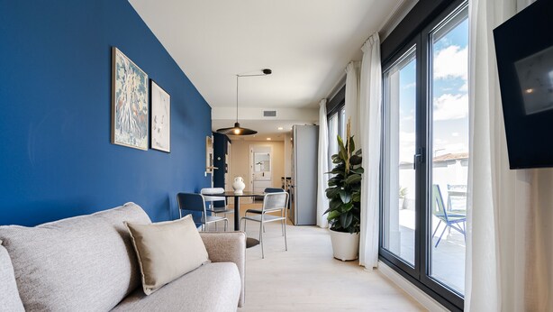 Un salon moderne avec un mur d’accent bleu, un canapé, un coin repas et de grandes fenêtres.
