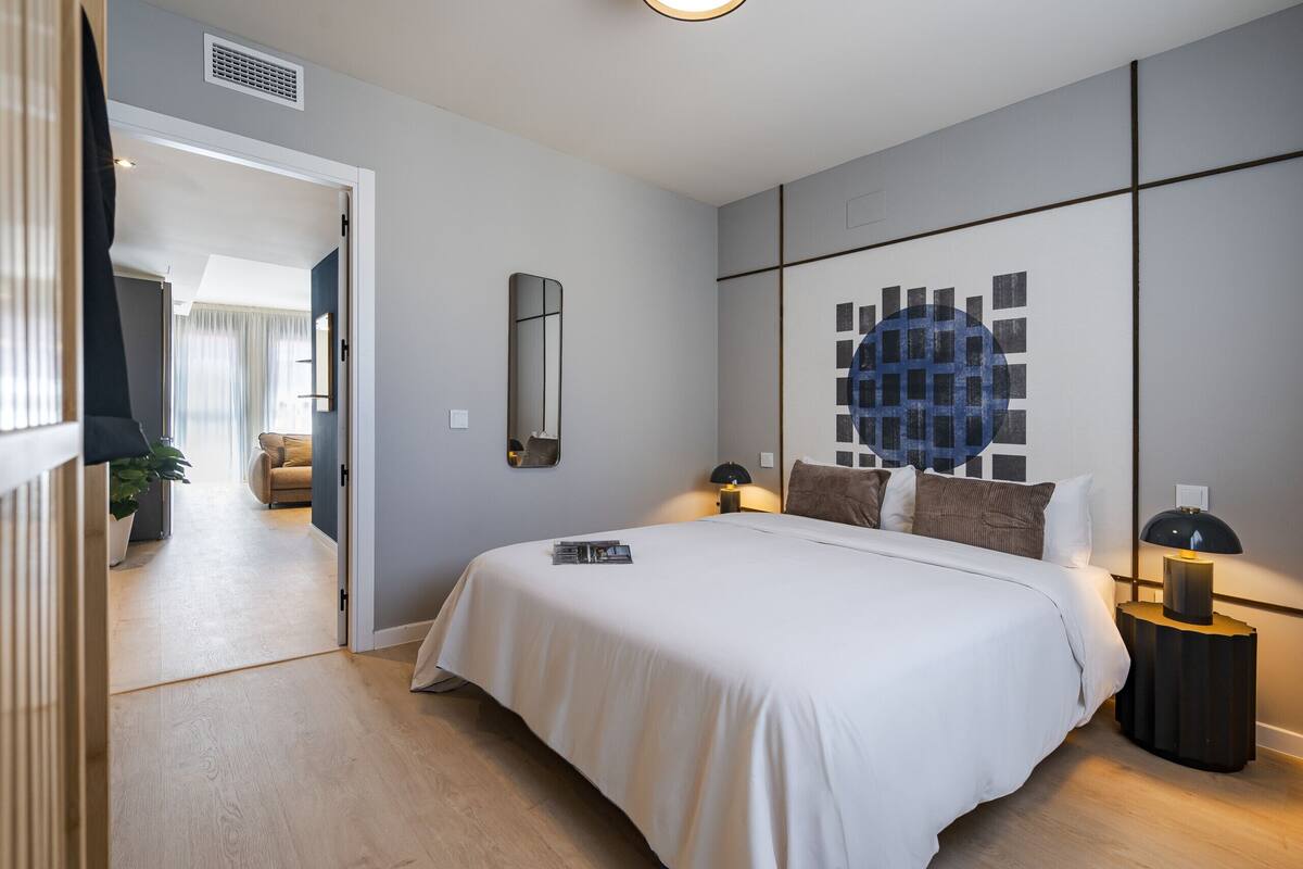 Une chambre moderne avec un grand lit, des tables de chevet, un miroir et une œuvre d’art murale.