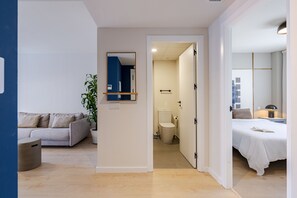 A modern room with a sofa, a potted plant, a mirror, and a bed with a book. - Puerto Alto Apartments by Olala Homes (Madrid)