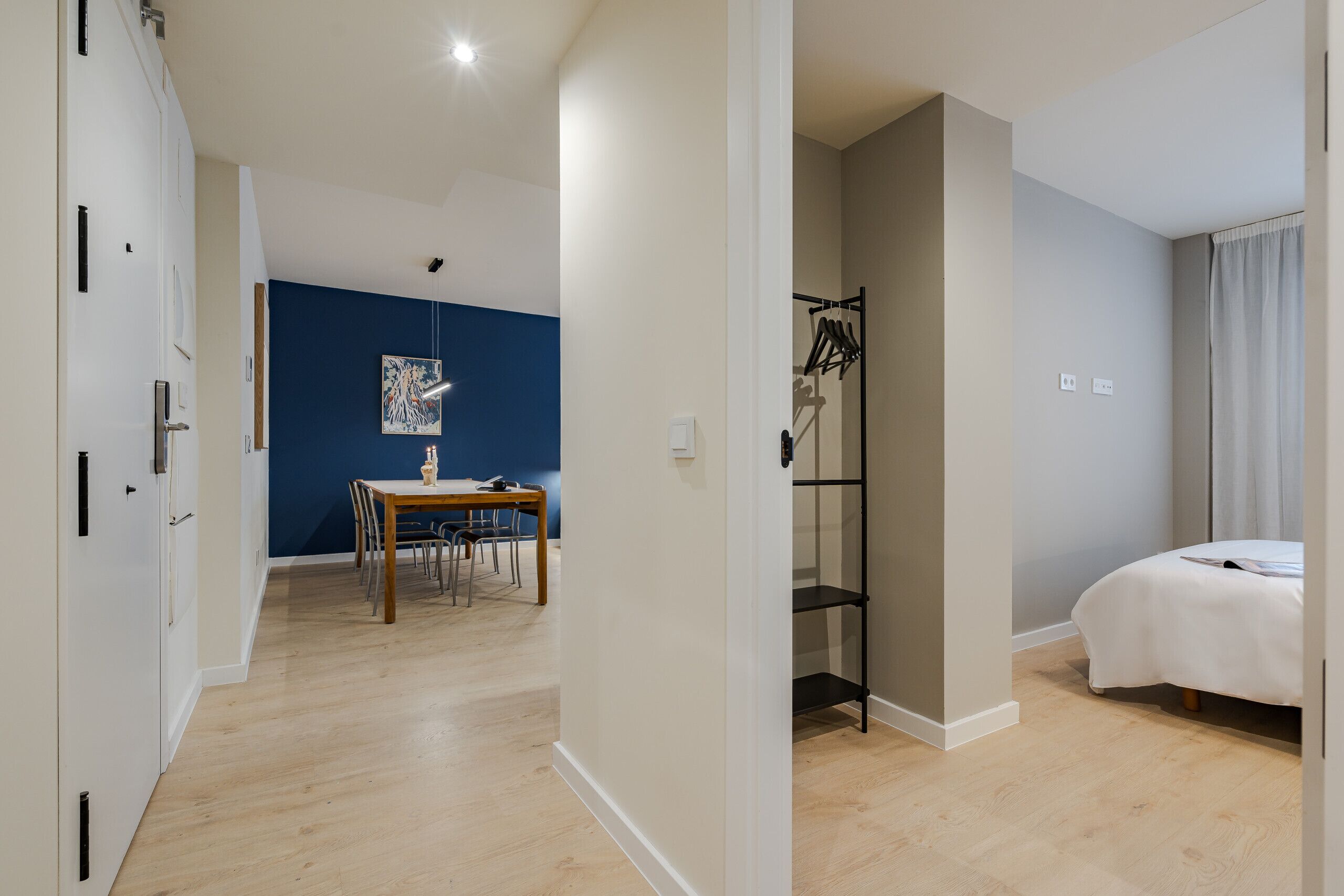 Ein modernes Hotelzimmer mit Holzboden, einem Bett, einem Schreibtisch mit Stühlen, einer blauen Akzentwand und einem Kleiderschrank.