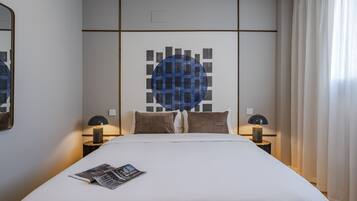 Una cama bien hecha con una revista, dos lámparas de noche y una obra de arte en la pared.