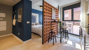 Une chambre d’hôtel moderne dotée d’une grande fenêtre, d’un lit, d’un coin cuisine et d’un espace salon avec des tabourets.