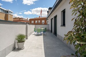 A narrow outdoor corridor with a potted plant and a table with chairs. - Puerto Alto Apartments by Olala Homes (Madrid)