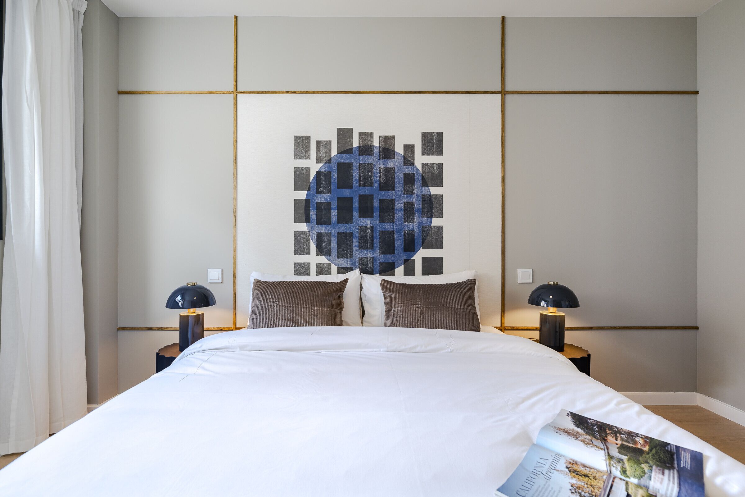 Un lit bien fait, avec une couette blanche et deux oreillers, un mur orné d’un motif géométrique et deux lampes de chevet.