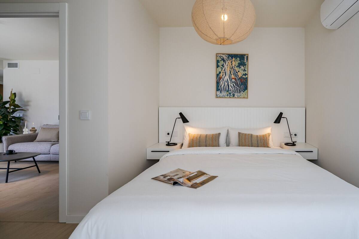 Une chambre moderne avec un grand lit, des lampes de chevet, une décoration murale et une petite table sur laquelle est posée une bougie.