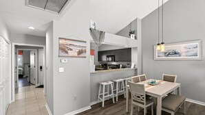 Une cuisine moderne avec des meubles de couleur sombre, un îlot central et des tabourets de bar. On y trouve une table à manger avec des chaises et un luminaire suspendu au-dessus.