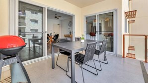 A modern outdoor dining area with a table and chairs, a barbecue grill, and a view of the interior through glass doors. - Darwin Inner City Oasis | 2 Bed Apt (Darwin City)